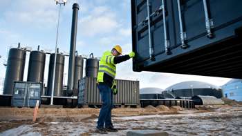 Mand i gult sikkerhedstøj og hjelm holder ved container, som bliver sænket på plads